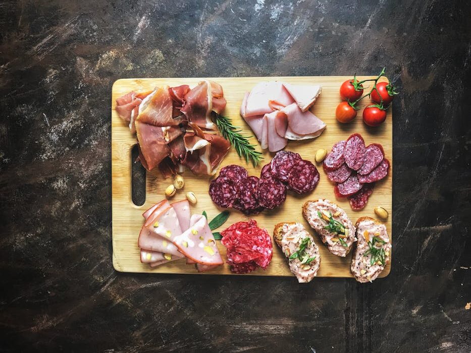 Delicious selection of cold cuts and bread on a wooden board with fresh herbs and tomatoes.